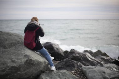 Bir kız deniz kenarındaki bir taşın üzerinde oturuyor..
