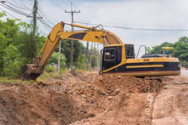 Yol onarımı için sokak asfaltındaki işçi izleme kazıcısı. Caddenin ortasında büyük bir kazıcı kazılmış çukurun yanında duruyor..