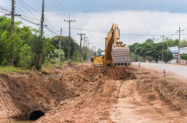 Yol onarımı için sokak asfaltındaki işçi izleme kazıcısı. Caddenin ortasında büyük bir kazıcı kazılmış çukurun yanında duruyor..