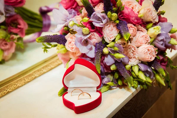 Bruids boeket en twee trouwringen in het rode vak in de vorm van een hart. — Stockfoto