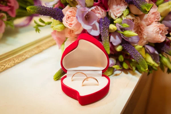 Bridal bouquet and two wedding rings in red box in the shape of a heart. — Stock Photo, Image