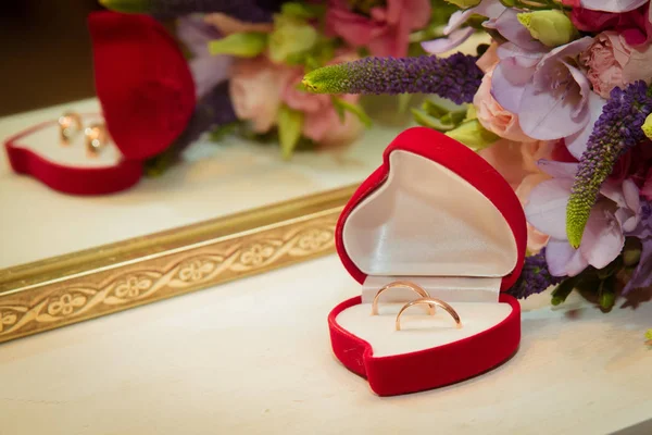 Bridal bouquet and two wedding rings in red box in the shape of a heart. — Stock Photo, Image