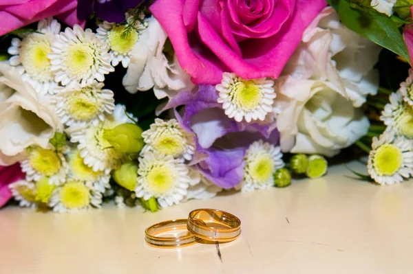 Χρυσά γαμήλια δαχτυλίδια που βρίσκονται κοντά σε λουλούδια — Φωτογραφία Αρχείου