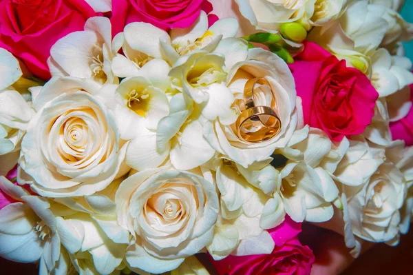 Gouden trouwringen liggen in de buurt van bloemen en rozen — Stockfoto