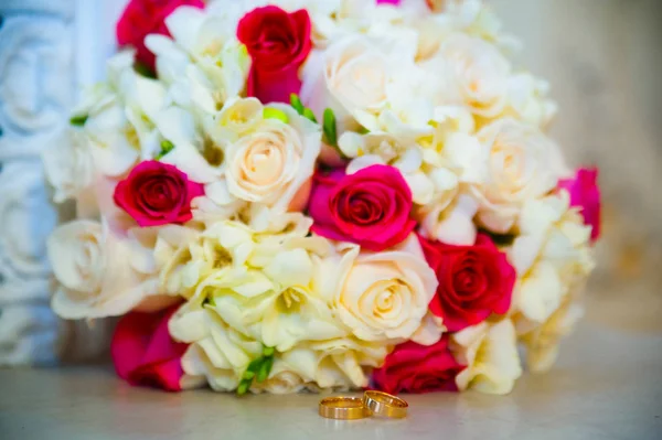 Złote obrączki ślubne, leżącego w pobliżu kwiaty i róże — Zdjęcie stockowe