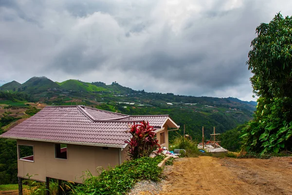 Silnice a domy ve vesnici na svazích hor s mraky. Sabah, Borneo, Malajsie — Stock fotografie