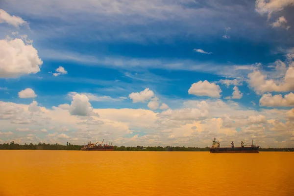 Lansekap dengan sungai kuning dan langit biru dengan awan. Sebuah kapal kargo berlayar di sungai. Malaysia, Kalimantan — Stok Foto