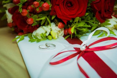 İki altın alyans yalan ve kırmızı gül buketi.