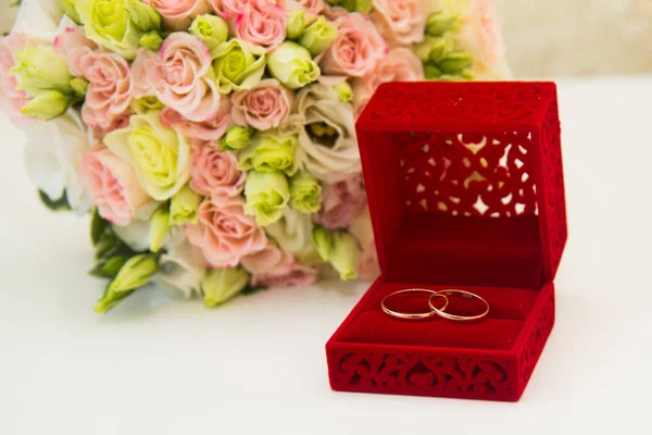 Gold wedding ring, a red box and a flower bouquet of the bride — Stock Photo, Image