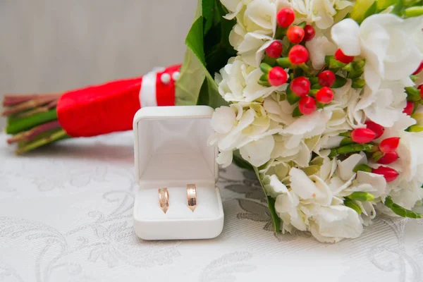 Dois anéis de casamento dourados em caixa branca e buquê com flores brancas e bagas vermelhas . — Fotografia de Stock