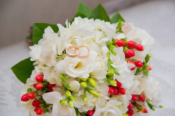 Two gold wedding rings lie on a bouquet with white flowers and red berries. — Stock Photo, Image