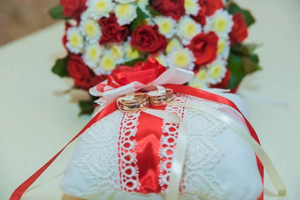 Two gold wedding rings lie and a bouquet of red roses. — Stock Photo, Image