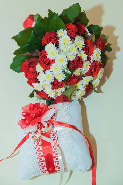 Two gold wedding rings lie and a bouquet of red roses. — Stock Photo, Image