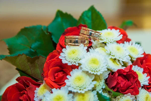 Dois anéis de casamento de ouro estão em um buquê com flores brancas e rosas vermelhas . — Fotografia de Stock