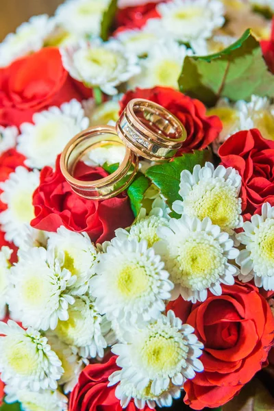 Dos anillos de boda de oro se encuentran en un ramo con flores blancas y rosas rojas . — Foto de Stock