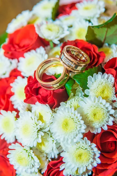 Due fedi nuziali d'oro si trovano su un bouquet con fiori bianchi e rose rosse . — Foto Stock