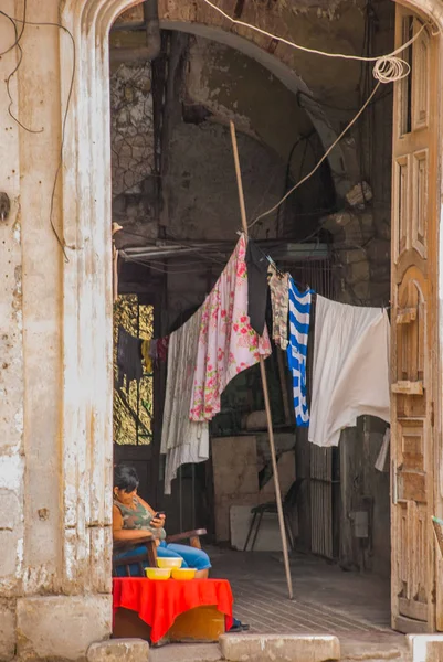 Old ruined building, open doors, hanging Laundry, woman sitting on chair and looking at the phone, buildings in downtown Havana. Cuba — Stock Photo, Image