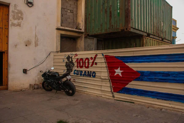 La motocicleta está aparcada cerca de la valla, donde se hacen los dibujos: la bandera de Cuba, graffiti en la valla con la inscripción 100 por ciento de La Habana. La Habana. Cuba . — Foto de Stock