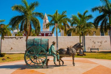 CAMPECHE, MEXICO: Statue of a horse drawn carriage in San Francisco de Campeche. A man sitting in a wagon with a barrel. next to the dog runs. clipart
