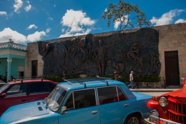 Holguin, Küba: Şehir merkezinde duvardaki büyük tarihsel rahatlama. Eski retro otomobil park