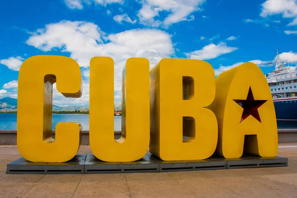 La inscripción de la CUBA. Enormes letras en el paseo marítimo, contra un cielo azul con nubes en Santiago de Cuba . — Foto de Stock