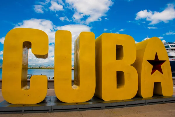 La inscripción de la CUBA. Enormes letras en el paseo marítimo, contra un cielo azul con nubes en Santiago de Cuba . — Foto de Stock