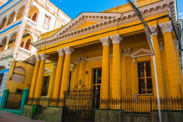 Żółty budynek w stylu klasycznym, z kolumny. Lokalnej ulicy z domami architektury kolonialnej. Santiago de Cuba, Kuba. — Zdjęcie stockowe