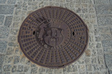 Krakow, Polonya: Pazar meydanındaki metal rögar kapağı üzerindeki eski Krakow kasabasının sembolü.