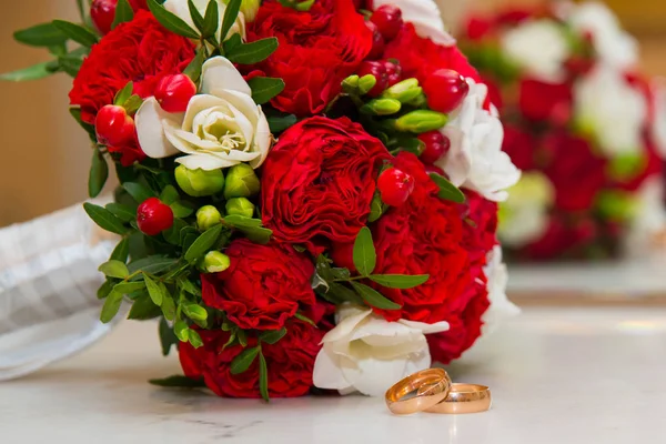 Valentijnsdag. Bruiloft.Trouwringen en een mooi boeket rode en witte bloemen. — Stockfoto