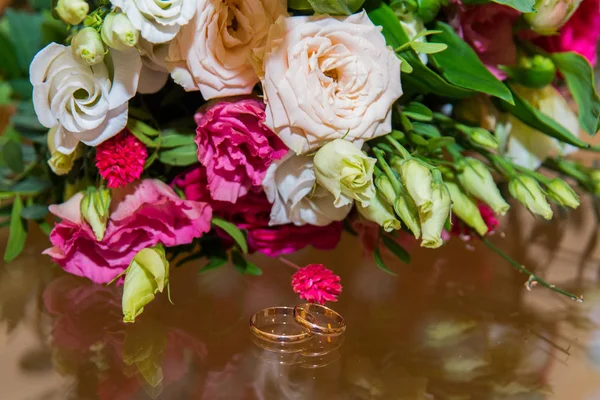 BODAS, Anillos y flores: Anillos de novia y ramo de rosas rojas y hermosas flores blancas — Foto de Stock