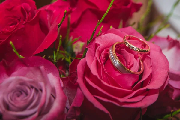 BODAS, Anillos y flores: Anillos de novia y ramo de rosas rojas . — Foto de Stock