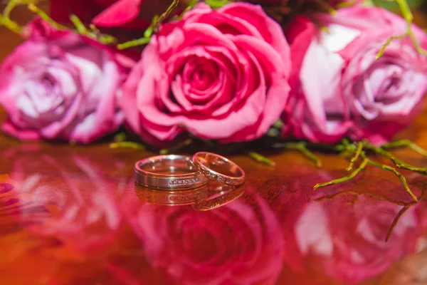 Svatba, prsteny a květiny: Svatební prsteny a svatební kytice z rudých růží. — Stock fotografie