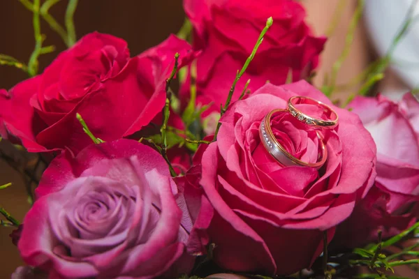 BODAS, Anillos y flores: Anillos de novia y ramo de rosas rojas . — Foto de Stock
