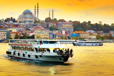 İstanbul, Türkiye: bulutlu güzel bir gün batımı, denizde hareket eden turistik tekneler, uzakta köprüyü ve aydınlık camileri görebilirsiniz. Süleyman Camii..