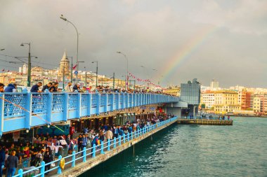 ISTANBUL, TURKEY - Ekim 2018: bulutlu havada Galata Köprüsü 'nden balık tutan insanlar. Aşağıda taze balıklı restoranlar var. Arka planda Galata kulesi ve gökkuşağı.