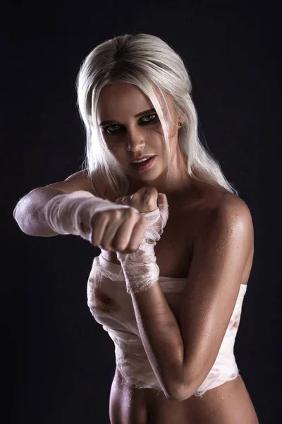 Beautiful young white-haired warrior girl with bandage on hands in light underwear on dark background. Portrait of a cute girl with a scar in white lingerie
