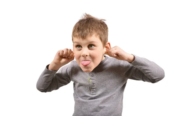 A small cheerful boy shows his tongue and pulls back his ears. A child makes a face on a white background Royalty Free Stock Photos