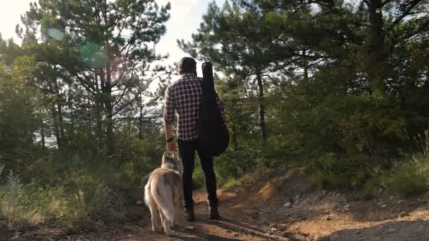 フォレスト内の つのシベリアン ハスキー犬を連れて歩いてギターを持つ男 — ストック動画