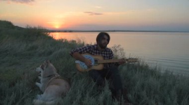 adam gitar Sibirya husky köpek ile yakın göl günbatımı ışık