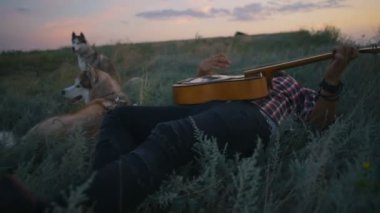 adam gitar iki Sibirya husky köpek ile yakın göl günbatımı ışık