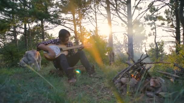 Mężczyzna Gra Gitarze Siedząc Psem Husky Syberyjski Pobliżu Ogniska Lesie — Wideo stockowe