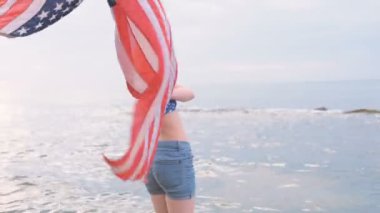 ABD bayrağı ile gündoğumu sırasında sahilde genç güzel kadın. 4 Temmuz kavramı
