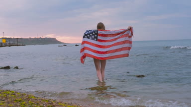 ABD bayrağı ile gündoğumu sırasında sahilde genç güzel kadın. 4 Temmuz kavramı