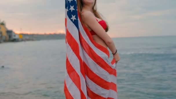 年轻美丽的女性在海滩在日出与美国旗子 7月4日概念 — 图库视频影像