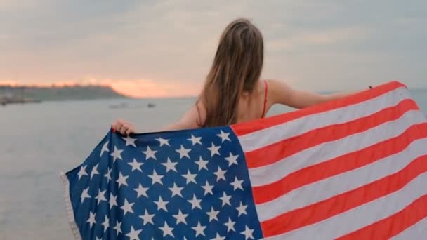 年轻美丽的女性在海滩在日出与美国旗子 7月4日概念 — 图库视频影像