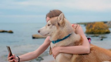Husky köpekle oynamayı sahilde günbatımı veya gündoğumu sırasında genç güzel kadın