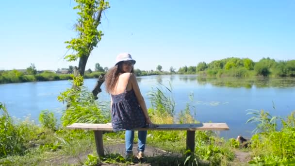 田舎で湖の近くに座っている若い女性 — ストック動画