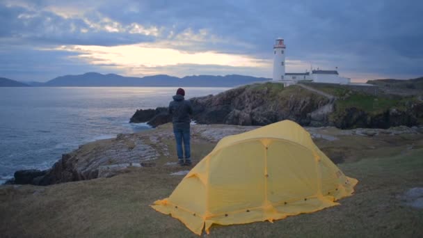 アイルランドの灯台の近くのテントを持つ男 — ストック動画