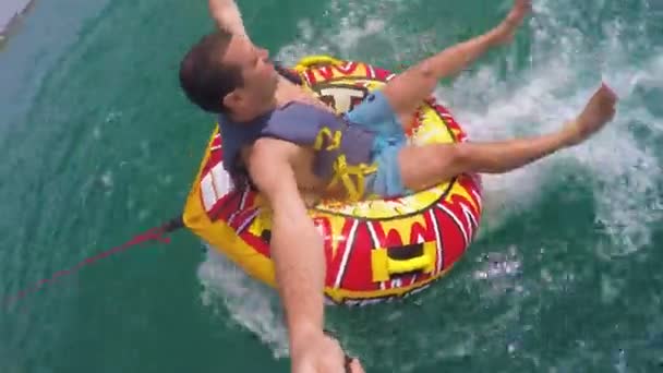 Hombre sentado en anillo inflable remolcado por un barco en el agua y grabándose con la cámara Go Pro — Vídeos de Stock