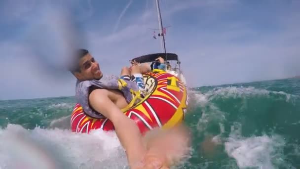 Человек, сидящий в надувном кольце, отбуксированный лодкой в воду и записывающий себя камерой Go Pro — стоковое видео